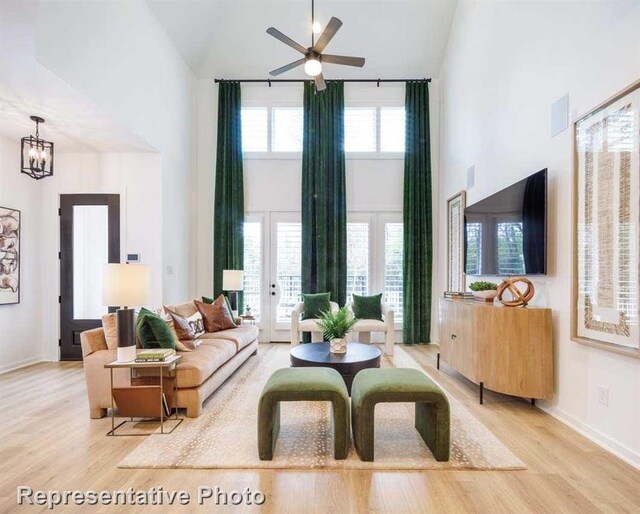 living room with ceiling fan with notable chandelier, high vaulted ceiling, and light hardwood / wood-style flooring