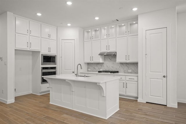 kitchen featuring oven, built in microwave, under cabinet range hood, white cabinetry, and a sink