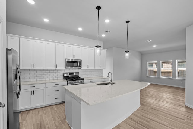 kitchen with white cabinets, hanging light fixtures, a kitchen island with sink, sink, and stainless steel appliances