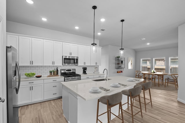 kitchen with hanging light fixtures, stainless steel appliances, a center island with sink, sink, and white cabinetry