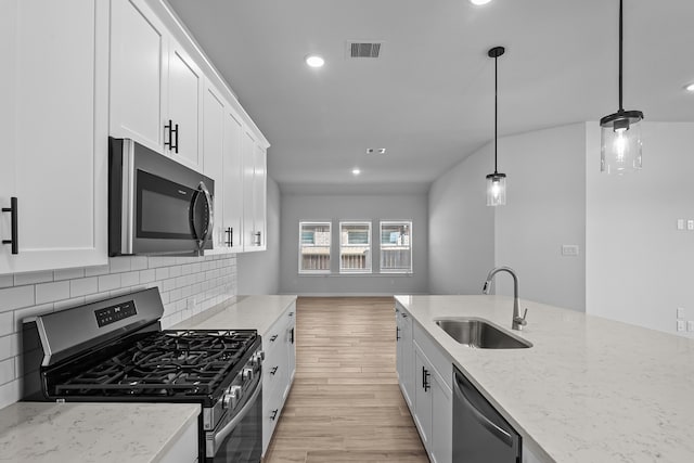 kitchen featuring light stone countertops, appliances with stainless steel finishes, sink, pendant lighting, and light hardwood / wood-style flooring