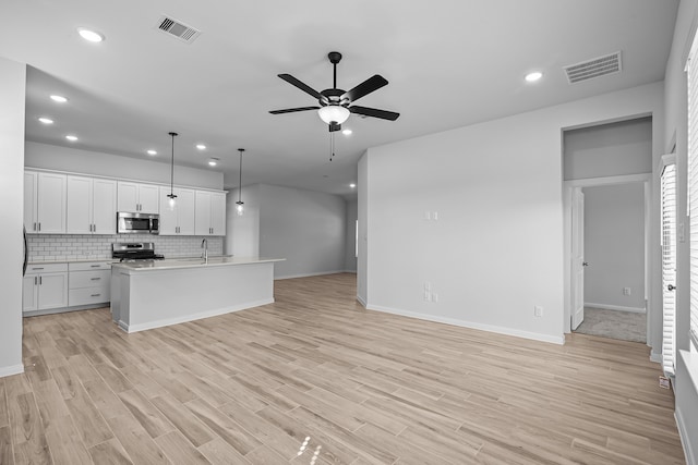 kitchen featuring an island with sink, hanging light fixtures, stainless steel appliances, white cabinets, and light hardwood / wood-style flooring