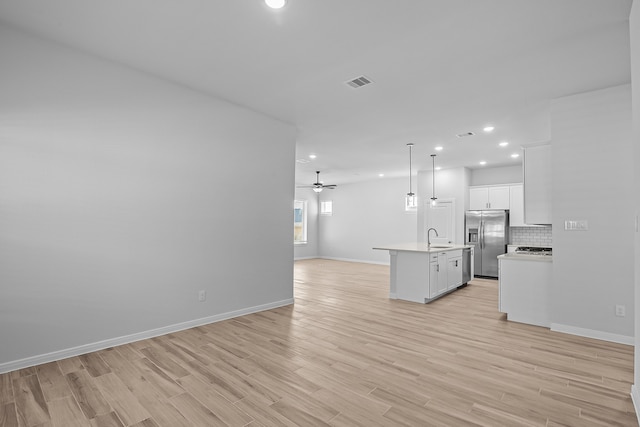 kitchen with light hardwood / wood-style flooring, stainless steel fridge, hanging light fixtures, and a center island with sink