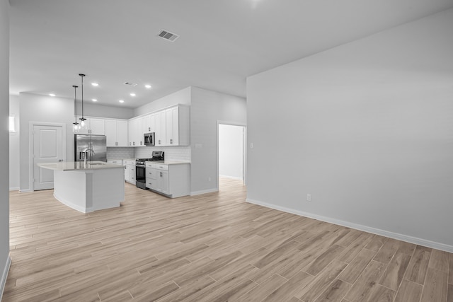 kitchen featuring appliances with stainless steel finishes, an island with sink, hanging light fixtures, white cabinetry, and light hardwood / wood-style flooring