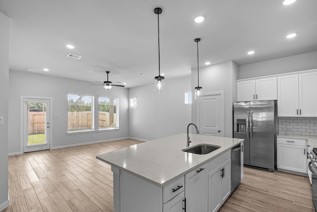 kitchen featuring light stone counters, white cabinetry, a kitchen island with sink, sink, and stainless steel appliances