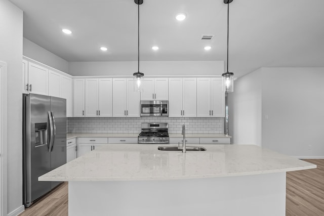 kitchen featuring stainless steel appliances, sink, decorative light fixtures, white cabinetry, and light hardwood / wood-style floors