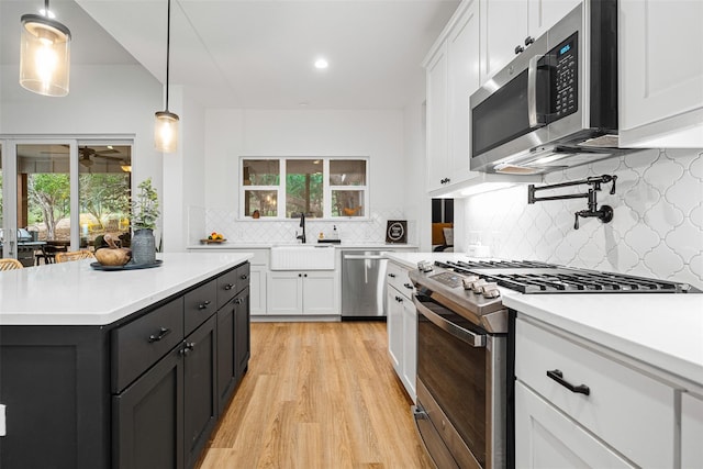 kitchen featuring pendant lighting, sink, white cabinets, light hardwood / wood-style floors, and stainless steel appliances