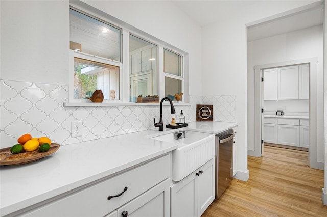 kitchen with white cabinetry, sink, stainless steel dishwasher, and light hardwood / wood-style flooring