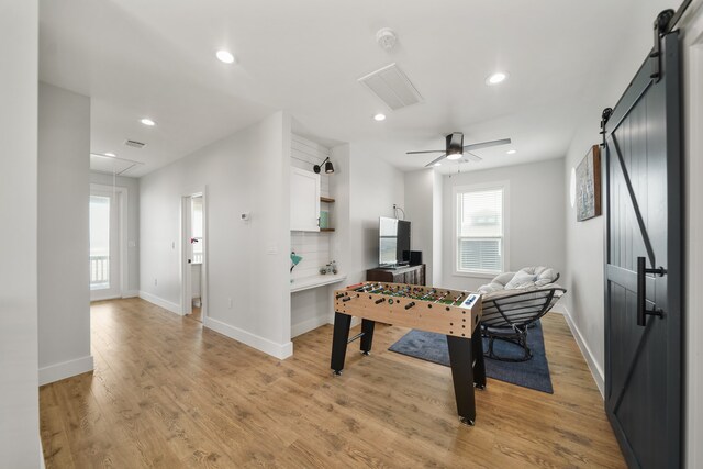 playroom with a barn door, light hardwood / wood-style flooring, and ceiling fan