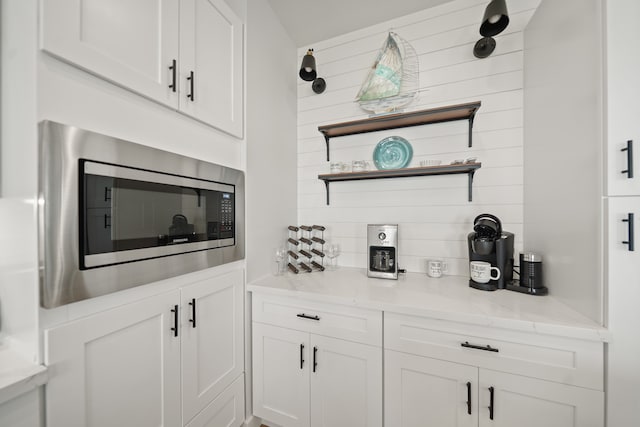 bar with stainless steel microwave, light stone counters, and white cabinets