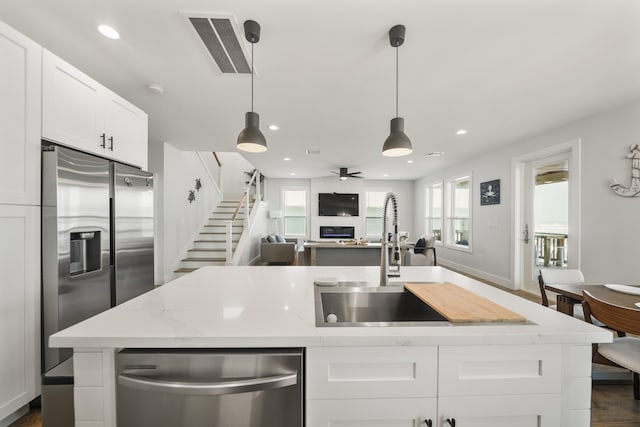 kitchen with decorative light fixtures, light stone counters, sink, white cabinets, and appliances with stainless steel finishes