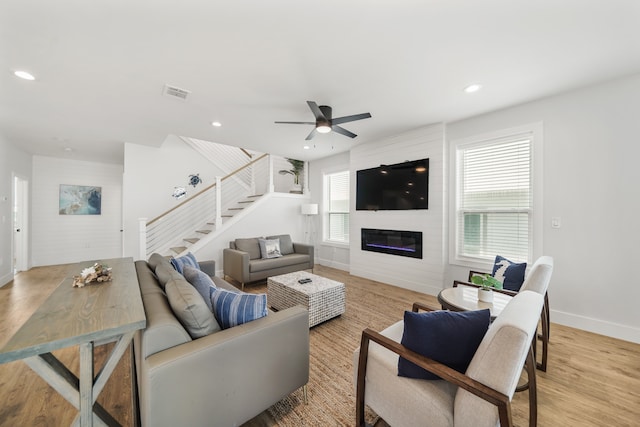 living room featuring ceiling fan, light hardwood / wood-style flooring, and a large fireplace