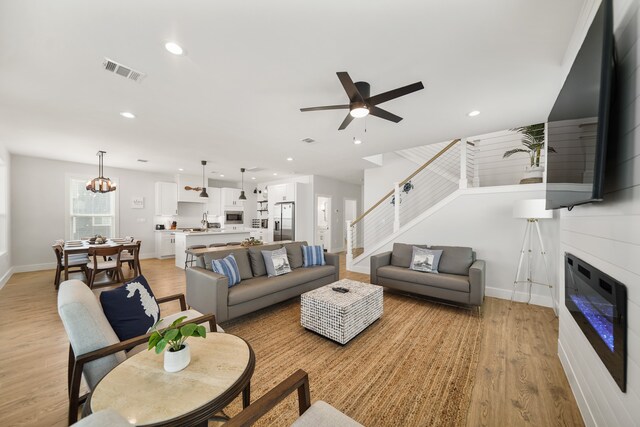 living room featuring ceiling fan with notable chandelier, light hardwood / wood-style flooring, and sink