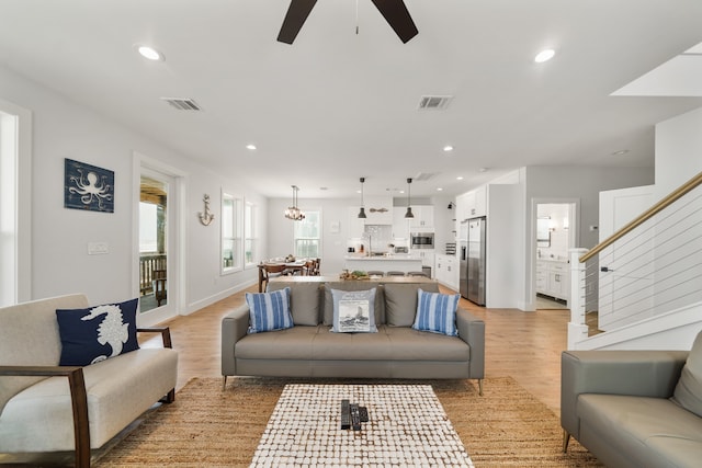 living room with ceiling fan with notable chandelier and light hardwood / wood-style floors