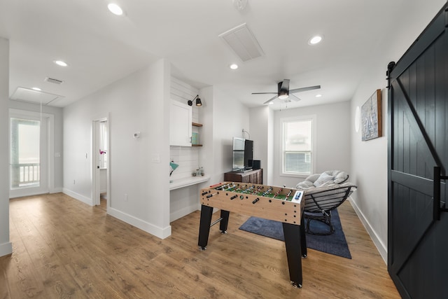 game room featuring ceiling fan, a barn door, and light hardwood / wood-style flooring