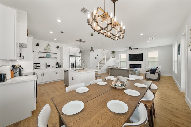 dining area with ceiling fan with notable chandelier, light wood-type flooring, and sink