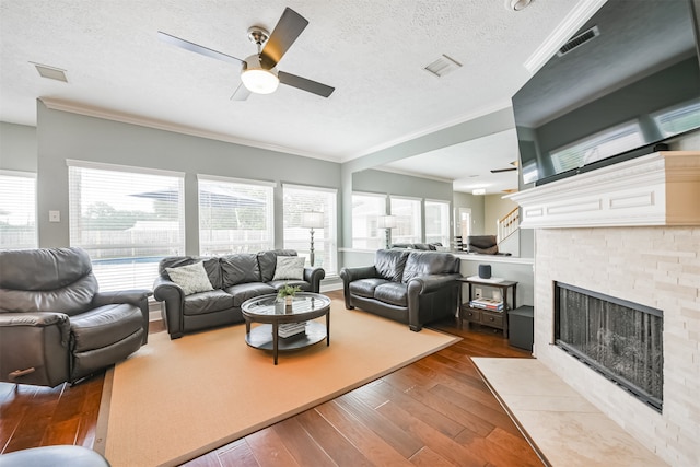 living room with ceiling fan, a textured ceiling, hardwood / wood-style flooring, a tile fireplace, and crown molding