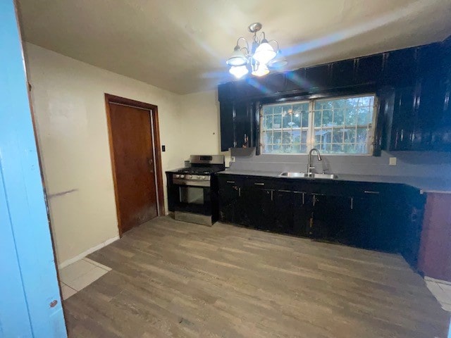 kitchen featuring stainless steel range with gas stovetop, light hardwood / wood-style floors, a notable chandelier, and sink