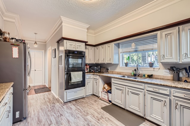 kitchen featuring stainless steel fridge, black double oven, sink, light hardwood / wood-style flooring, and a textured ceiling