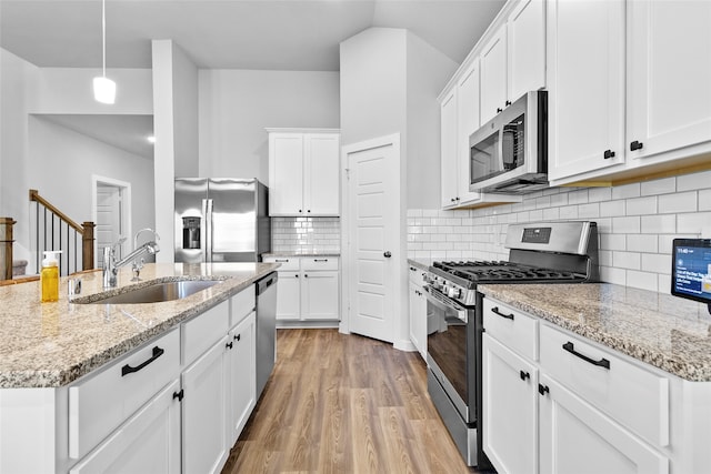 kitchen featuring white cabinets, appliances with stainless steel finishes, decorative light fixtures, and light hardwood / wood-style flooring