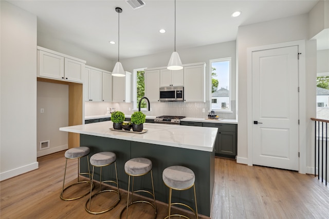 kitchen with a kitchen island, light hardwood / wood-style floors, stainless steel appliances, decorative light fixtures, and white cabinets