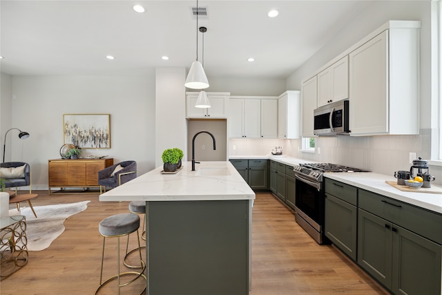 kitchen featuring appliances with stainless steel finishes, white cabinets, a center island with sink, and light wood-type flooring