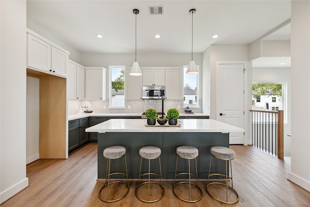 kitchen with light hardwood / wood-style flooring, decorative light fixtures, a kitchen island, and white cabinets