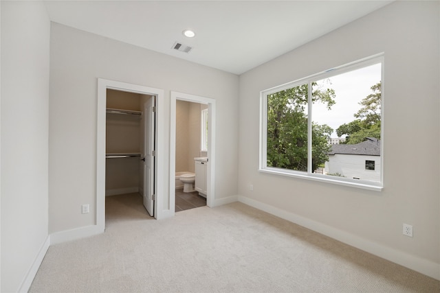 unfurnished bedroom featuring light carpet, a walk in closet, a closet, and ensuite bath