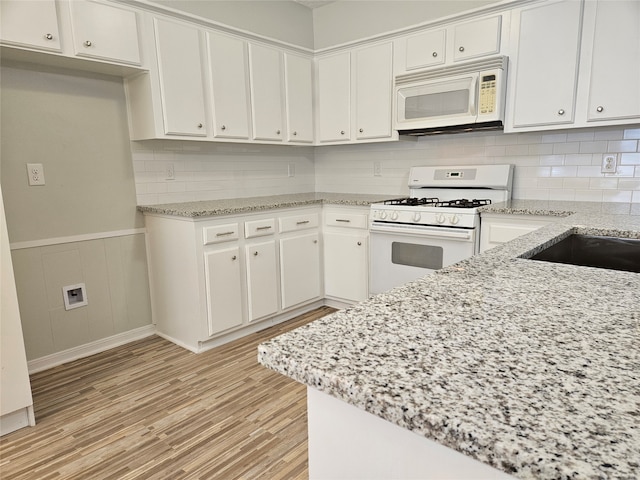 kitchen with light stone countertops, white cabinets, white appliances, and light hardwood / wood-style floors