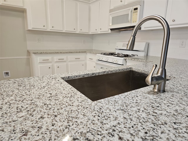 kitchen featuring sink, light stone countertops, white cabinetry, white appliances, and tasteful backsplash