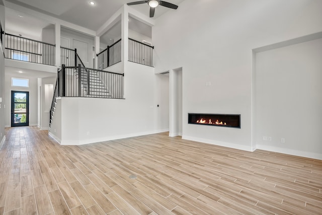 unfurnished living room with a towering ceiling, light hardwood / wood-style floors, and ceiling fan