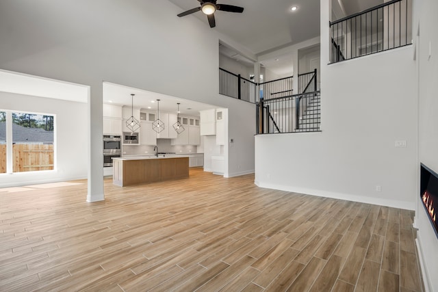 unfurnished living room with light hardwood / wood-style floors, sink, a high ceiling, and ceiling fan