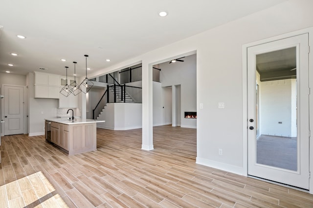 kitchen with decorative backsplash, white cabinetry, a kitchen island with sink, light wood-type flooring, and decorative light fixtures