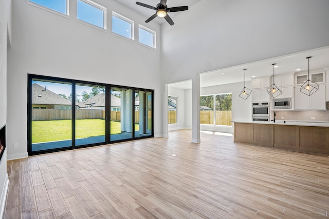 unfurnished living room featuring a high ceiling, light wood-type flooring, and ceiling fan