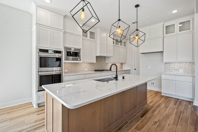 kitchen with an island with sink, appliances with stainless steel finishes, white cabinetry, decorative light fixtures, and sink