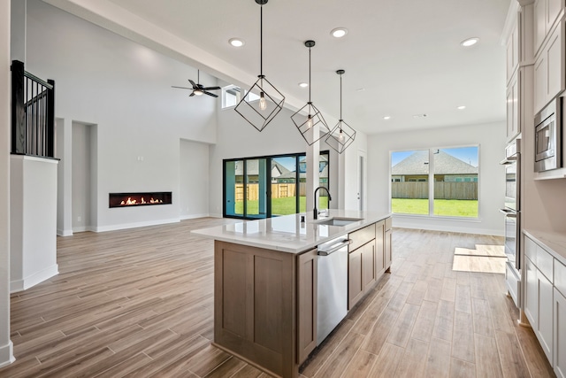 kitchen with sink, an island with sink, hanging light fixtures, white cabinetry, and stainless steel appliances