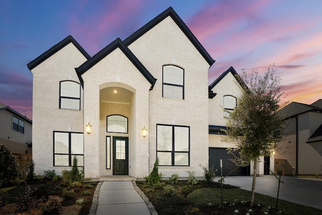 french provincial home with an attached garage, driveway, and brick siding