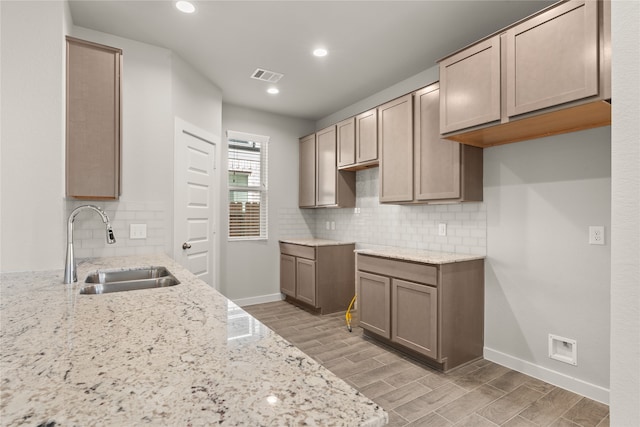 kitchen with light wood-type flooring, light stone counters, sink, and backsplash