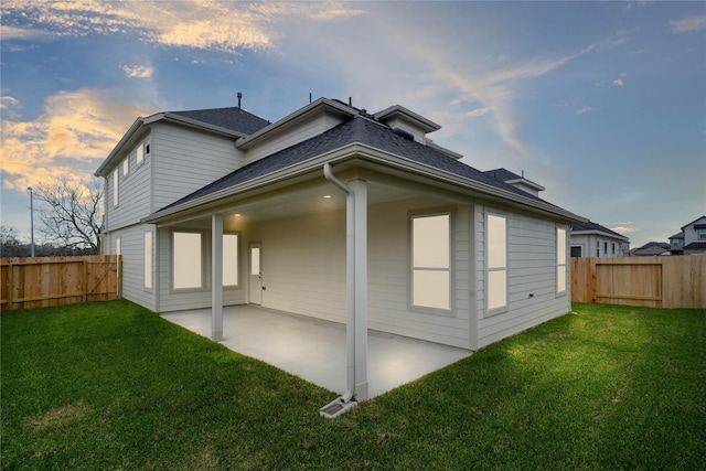 back of property at dusk featuring a patio area, a lawn, and a fenced backyard