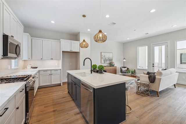 kitchen featuring an island with sink, stainless steel appliances, sink, decorative light fixtures, and white cabinetry