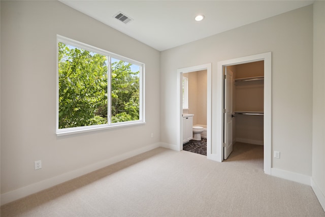 unfurnished bedroom with ensuite bathroom, multiple windows, a spacious closet, and light colored carpet