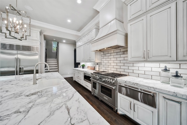 kitchen with premium range hood, tasteful backsplash, premium appliances, sink, and pendant lighting