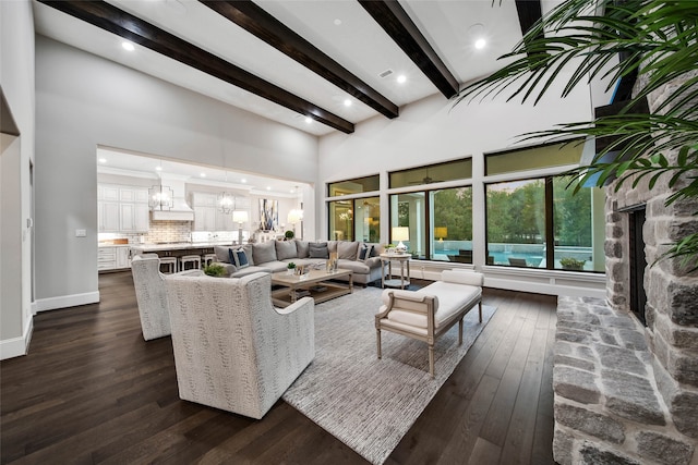 living room with a stone fireplace, a towering ceiling, beam ceiling, dark hardwood / wood-style flooring, and a chandelier