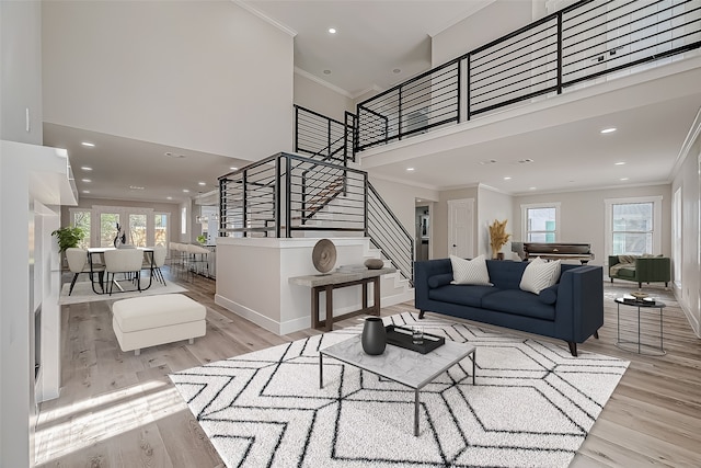 living room with a towering ceiling, crown molding, light hardwood / wood-style floors, and a healthy amount of sunlight