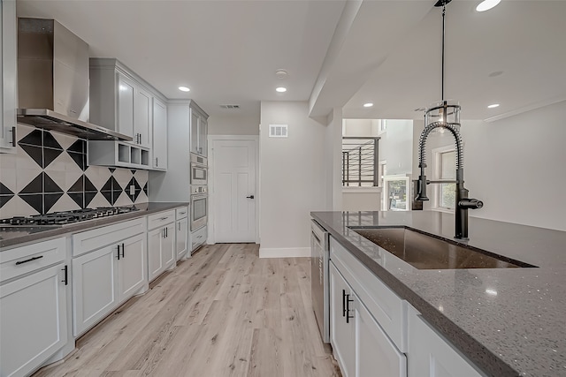 kitchen with sink, light hardwood / wood-style floors, wall chimney exhaust hood, white cabinets, and dark stone countertops