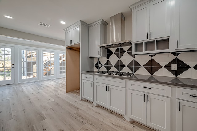 kitchen with french doors, decorative backsplash, wall chimney range hood, light wood-type flooring, and stainless steel gas stovetop