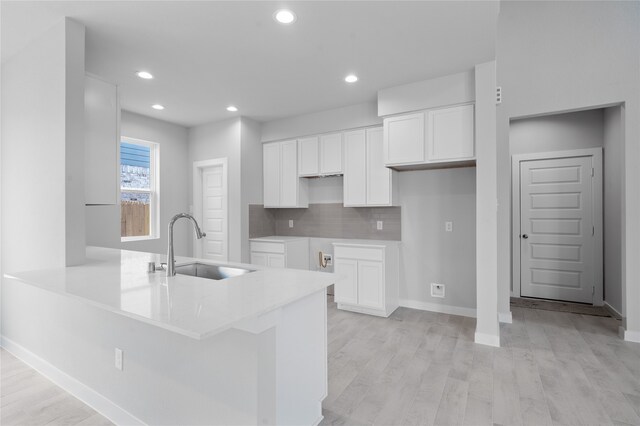 kitchen featuring white cabinets, decorative backsplash, kitchen peninsula, sink, and light hardwood / wood-style flooring