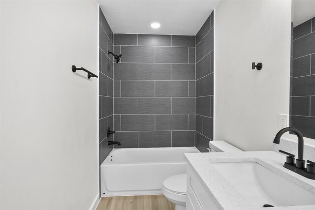 full bathroom featuring vanity, hardwood / wood-style floors, tiled shower / bath, and toilet