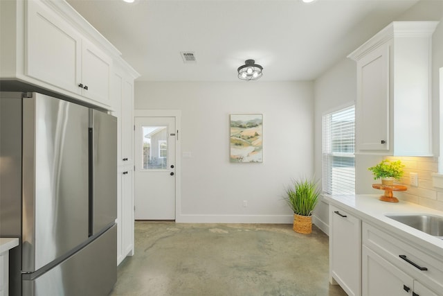 kitchen with stainless steel refrigerator, white cabinetry, sink, and backsplash