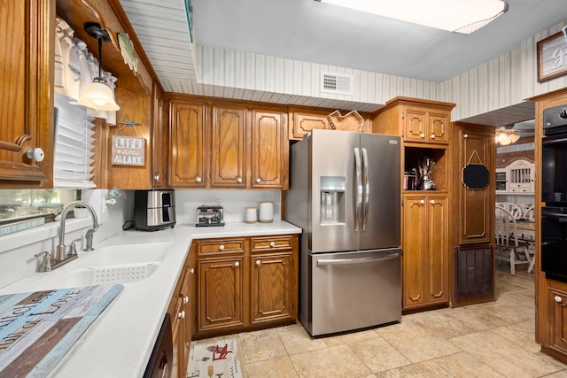 kitchen with hanging light fixtures, ceiling fan, double oven, stainless steel refrigerator with ice dispenser, and sink